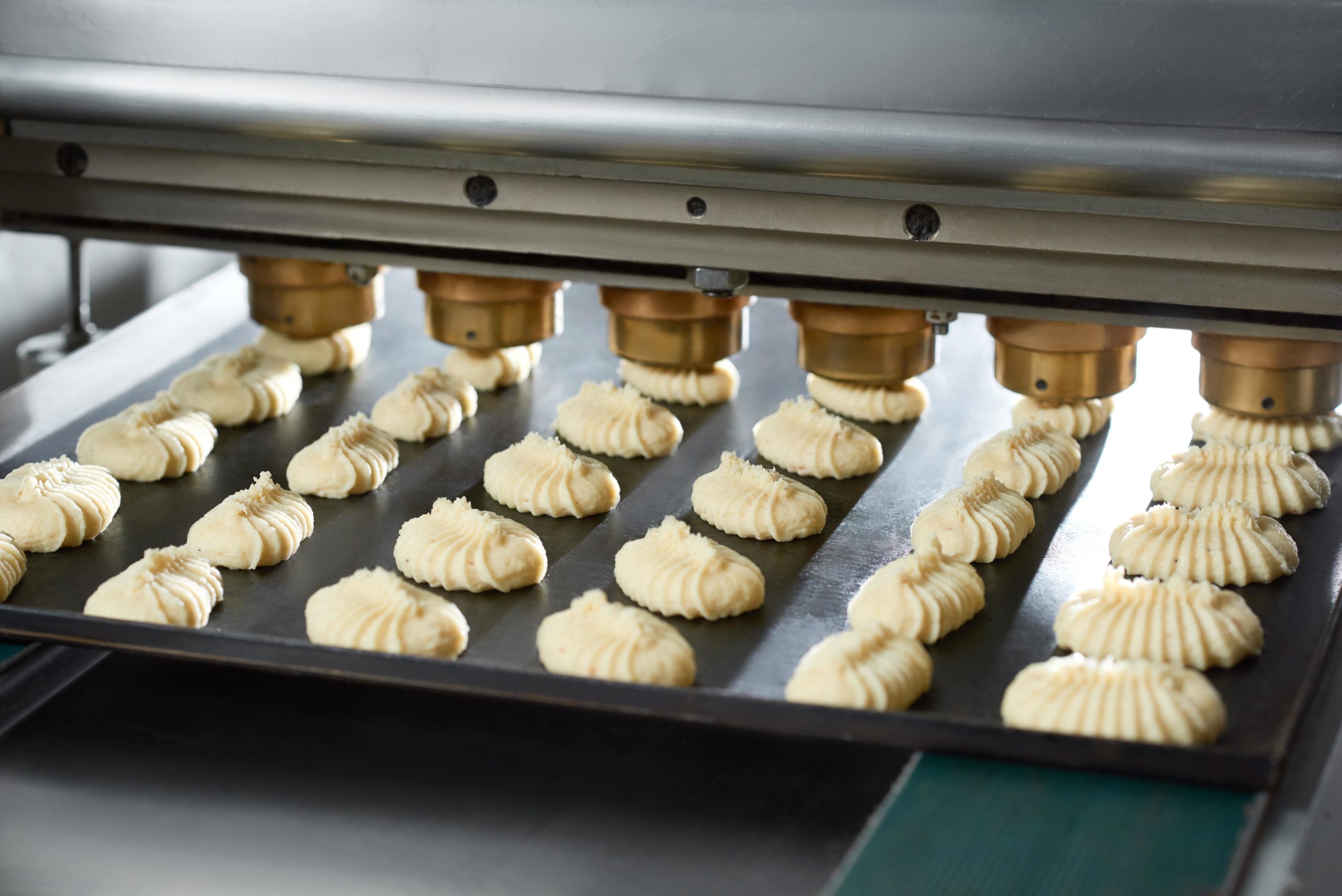 close-up-conveyor-line-s-equipment-making-little-identical-cakes-from-raw-dough-they-lie-black-dish-conveyor-line-bakery-min