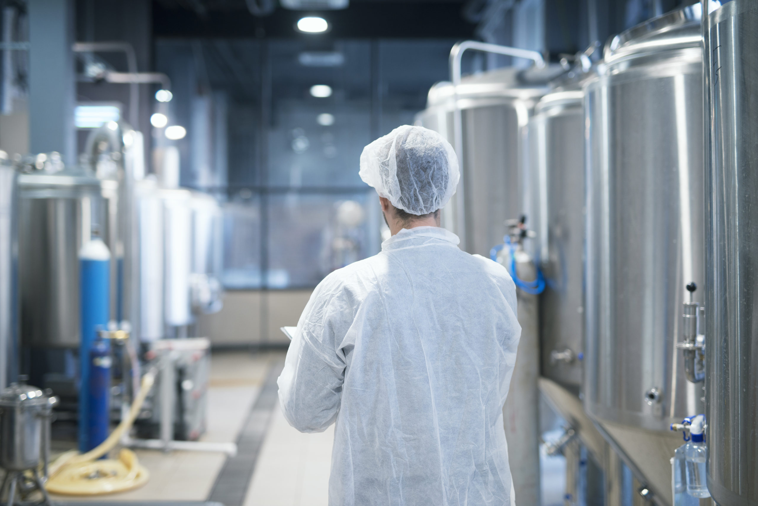 Technologist in white protective suit walking through food factory production line checking quality.